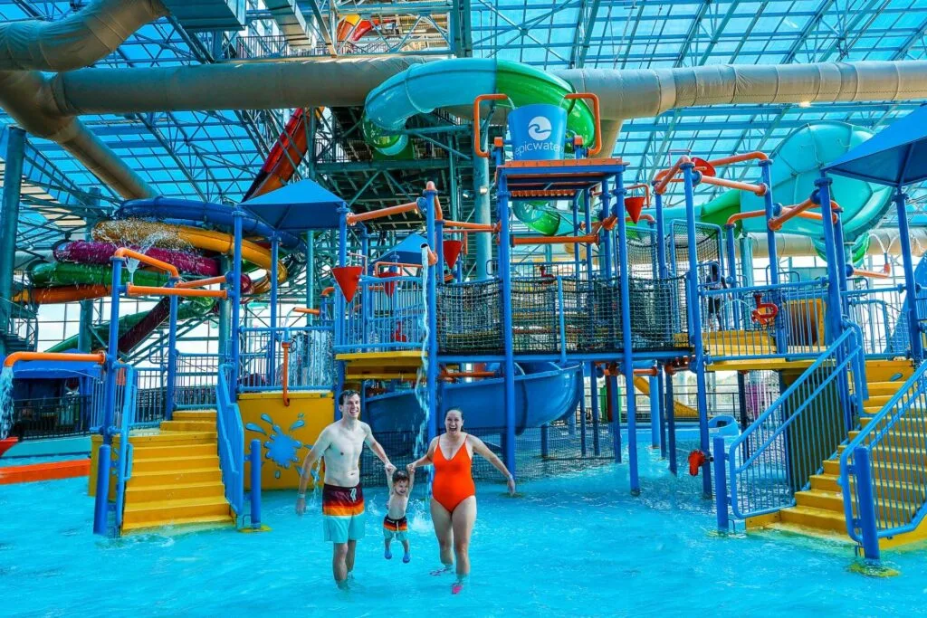 Epic Waterpark in Grand Prairie, Texas. A family swimming their son in front of a huge indoor aquatic playground in Dallas with a dump bucket and slides.