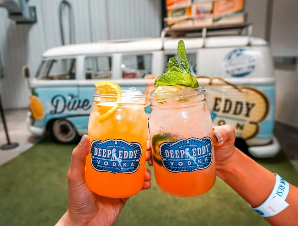 Two Deep Eddy Vodka mason jar glasses filled with a cocktail with a Volkswagen bus in the background. 
