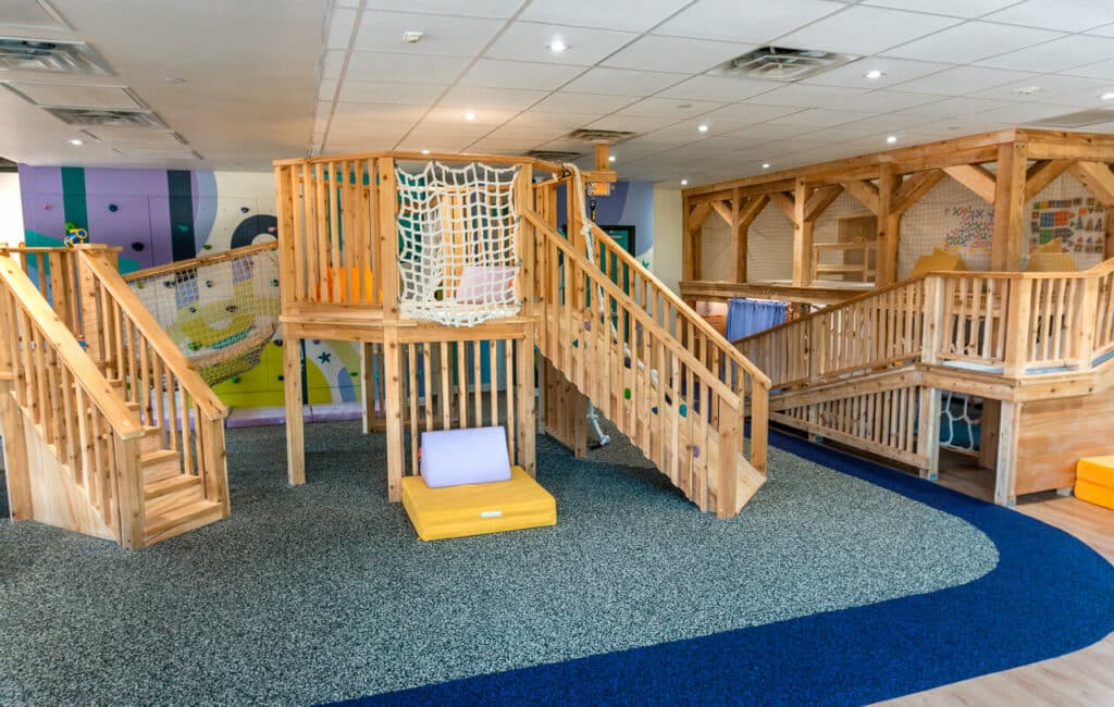 A beautiful natural wood indoor play fort with a colorful rock wall in the back at Bright Side Play.