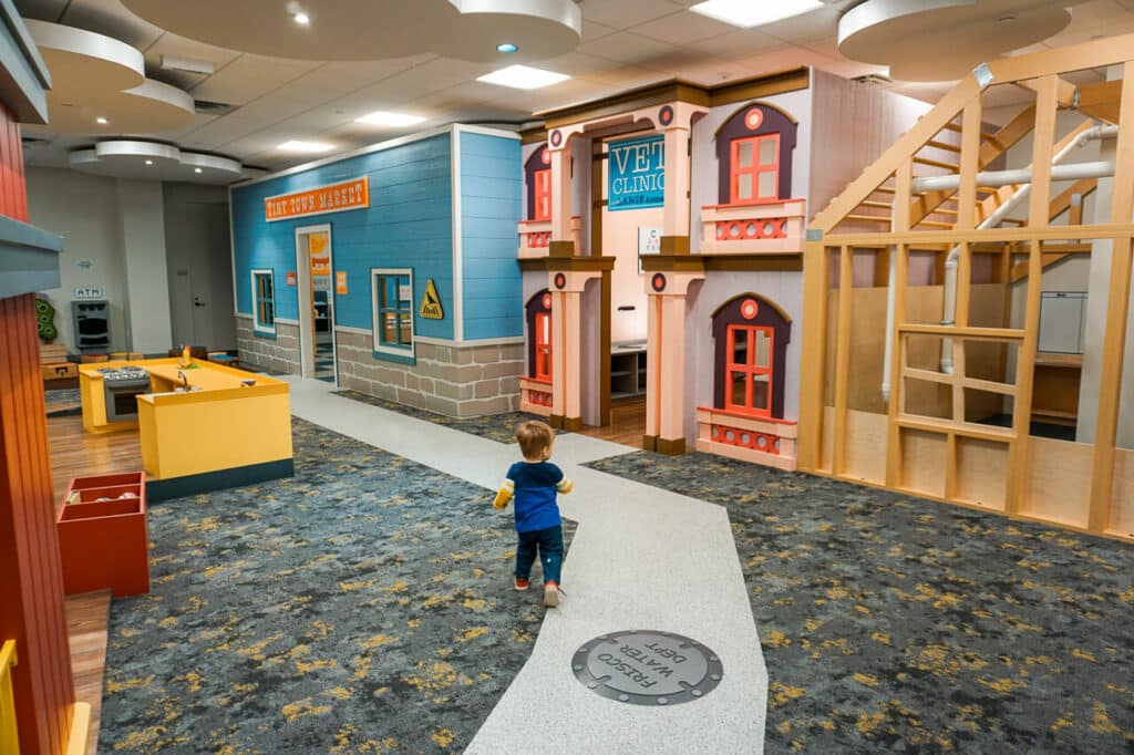 A toddler boy walking through Frisco Public Library's indoor play area.
