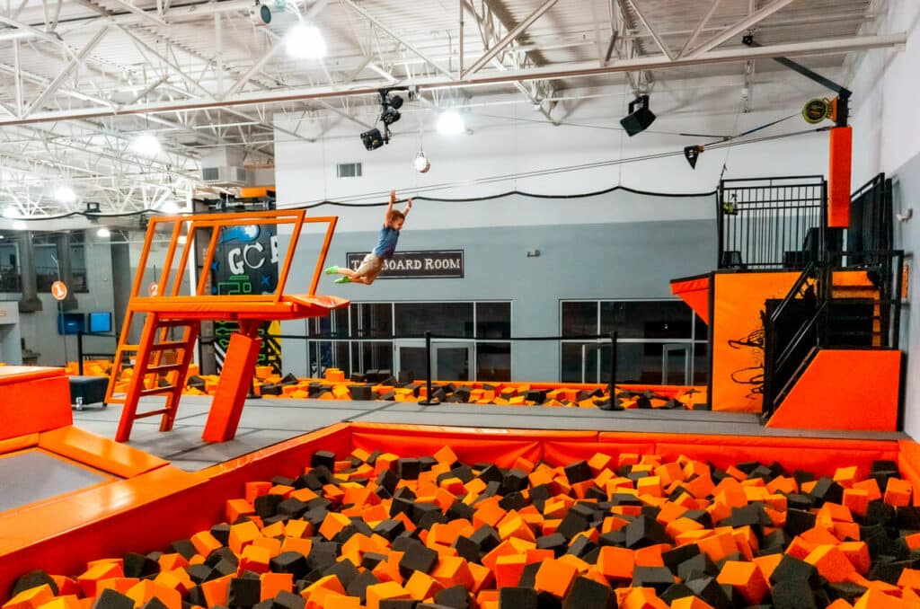 A young boy jumping from a platform and into a giant orange and black foam pit at Ground Control - one of the best indoor trampoline parks in Dallas.