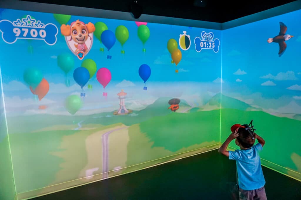 A young boy inside an Immersive Gamebox room playing Paw Patrol, popping balloons.