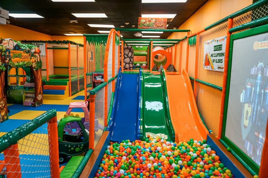 A blue, green, and orange slide going into a colorful ball pit inside an indoor playground in Dallas. Located at Jungle Castle.