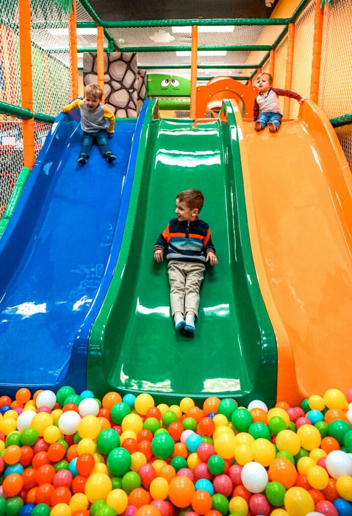 Three young boys going down racing slides into a ball pit at an indoor playground in Dallas.
