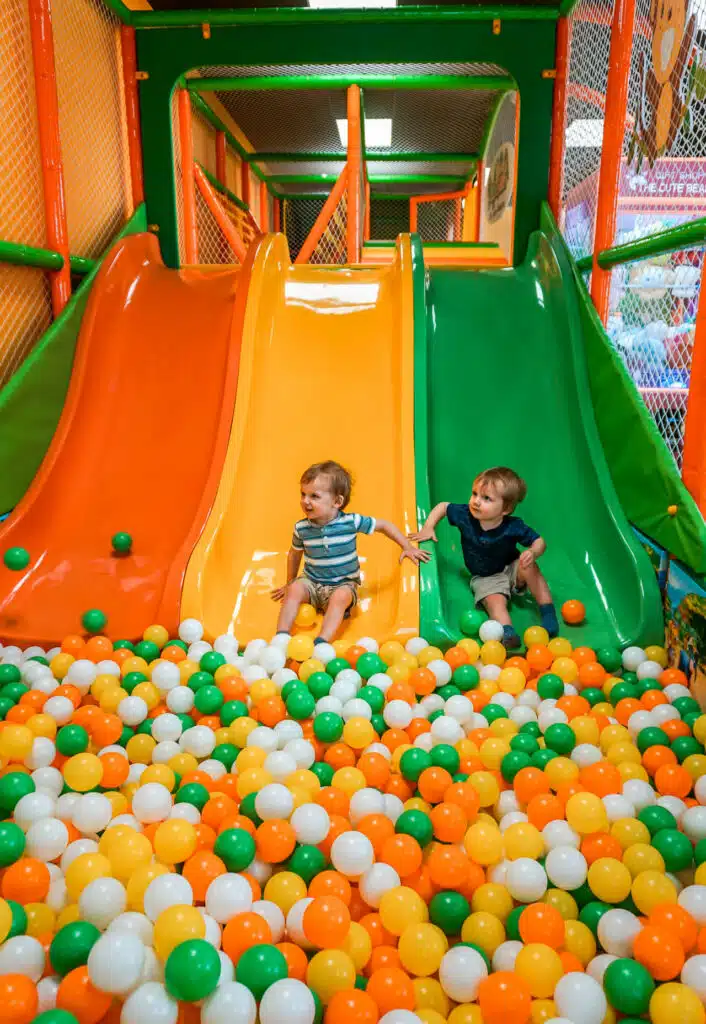 Twin toddler boys going down a yellow and green slide and into a ball pit at Jungle Land—an indoor playground in Dallas.