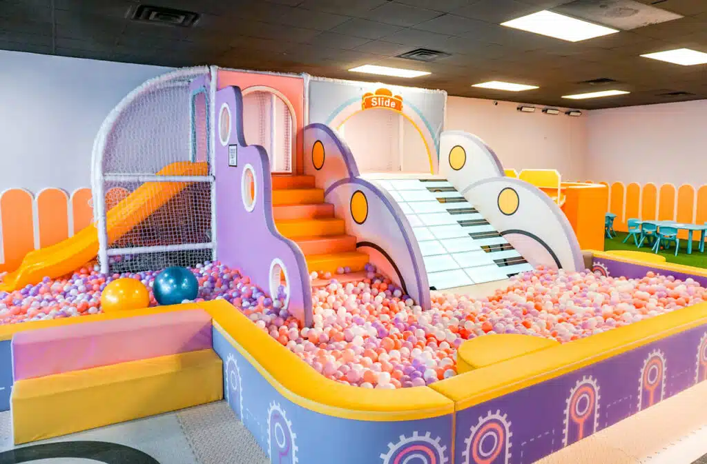 A purple and yellow indoor playground with stairs, a wide keyboard slide, and a ball pit at Mini Playtime in Dallas. 