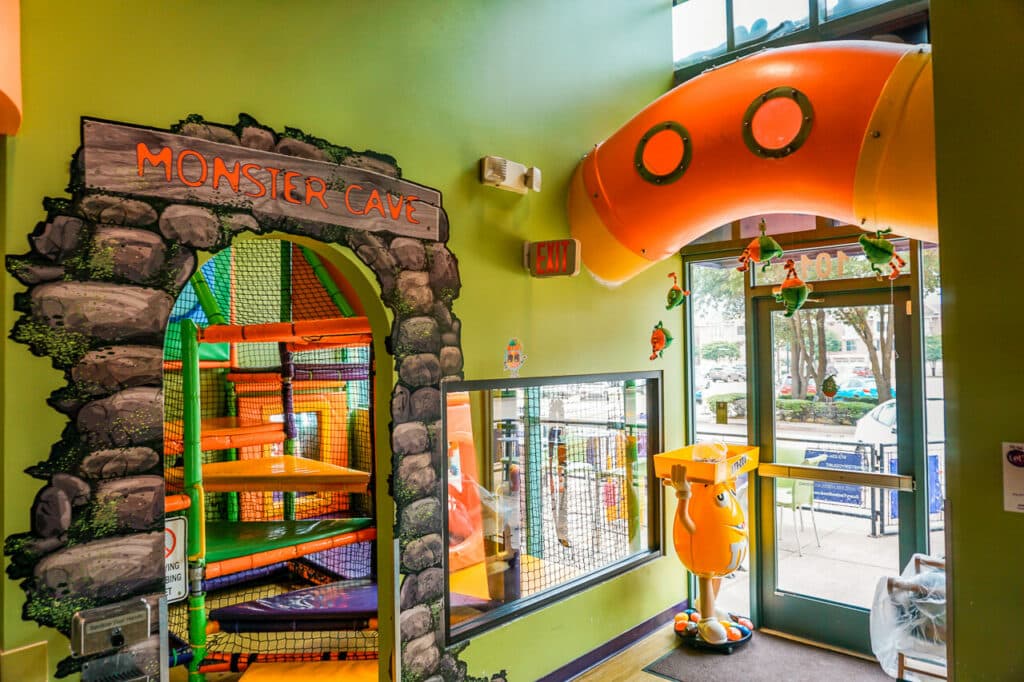 An indoor playground inside a "monster cave" with an orange tunnel bridge that goes to the other side of the room located at Monster Yogurt in Dallas.