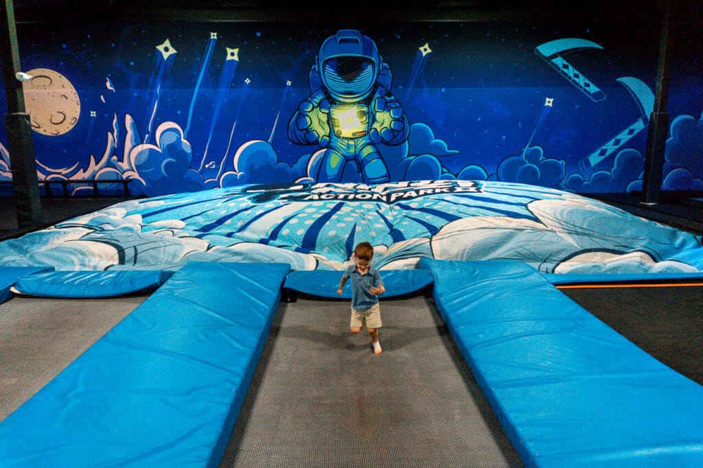 A young boy jumping on a trampoline with a giant airbag cloud and astronaut in the background from Ninja Kidz Action Park.