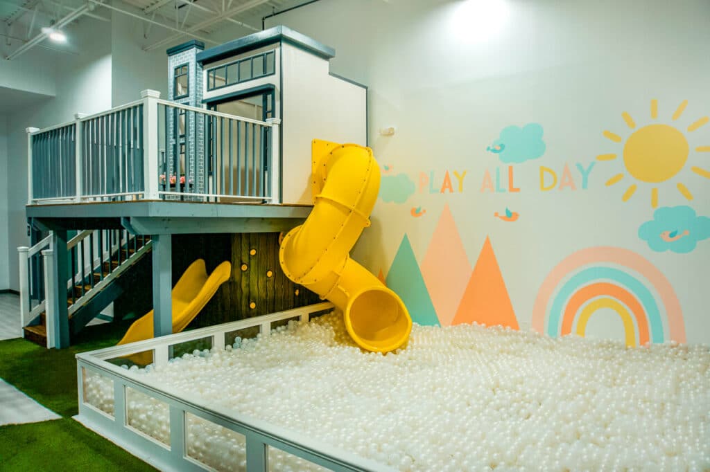 an indoor playground in Dallas with a white treehouse and a yellow slide going into a giant ball pit. Located at PeeknPlay. 