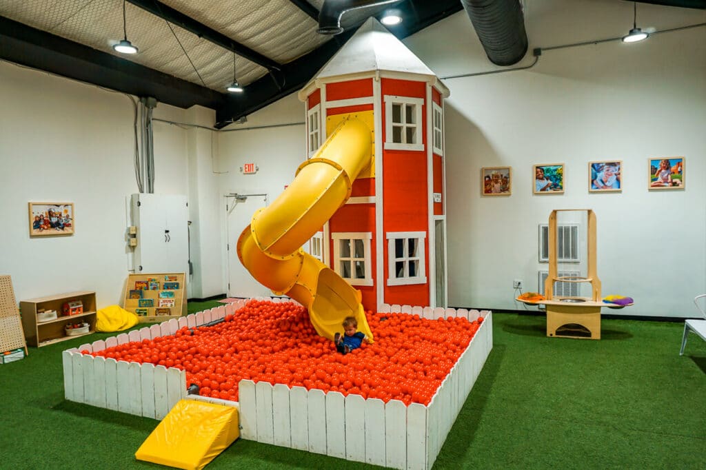 A little boy going down a slide and into a red ball pit at an indoor playground in Dallas — Project Play Discovery Museum.