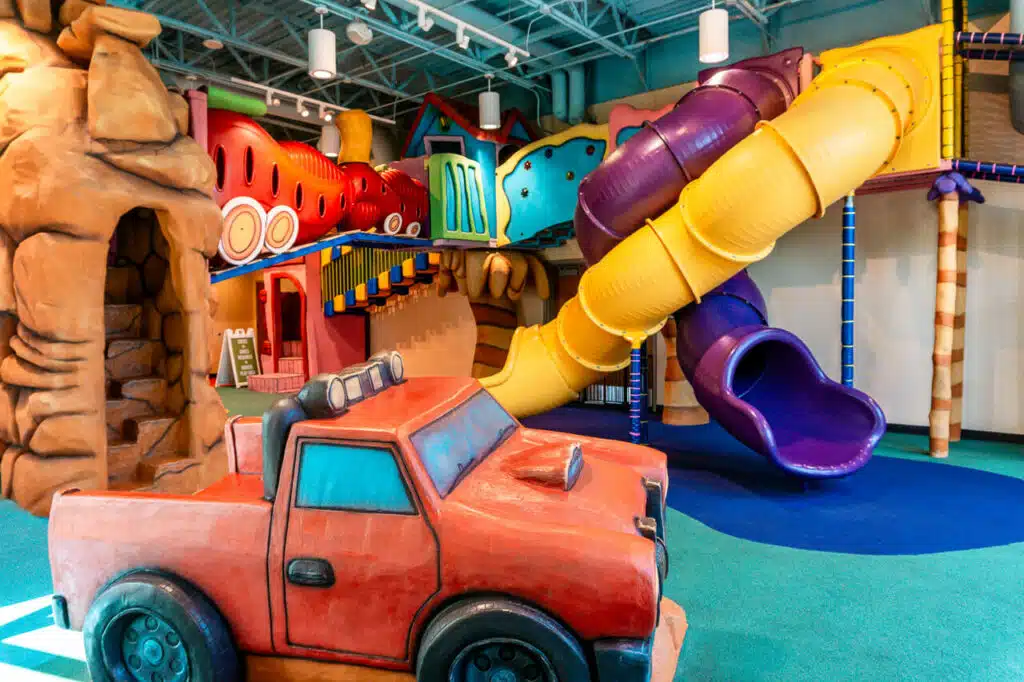 A whimsical indoor playground in Dallas with twisting slides, a red truck, and tunnels at The Rec of Grapevine.