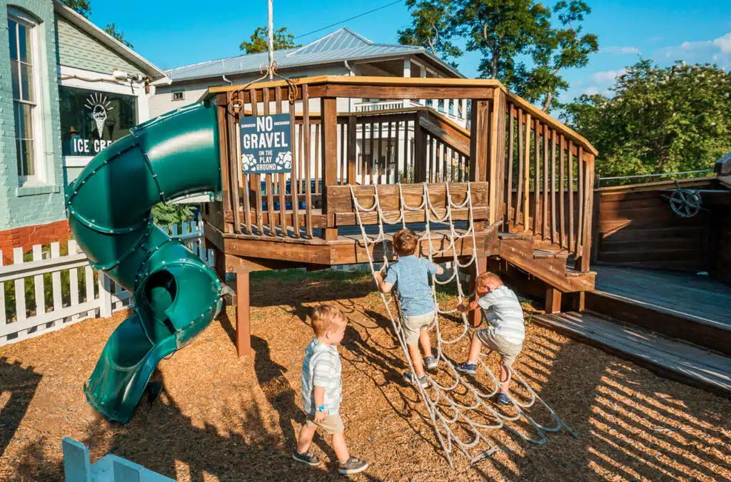 Two boys climbing a rope ladder to play on a playground shaped like pirate ship located at TinTop Burgers in New Braunfels, Texas.