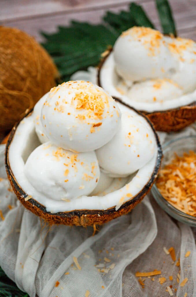 Two fresh coconut shells filled with four scoops of homemade Coconut Sorbet with toasted coconut on top.