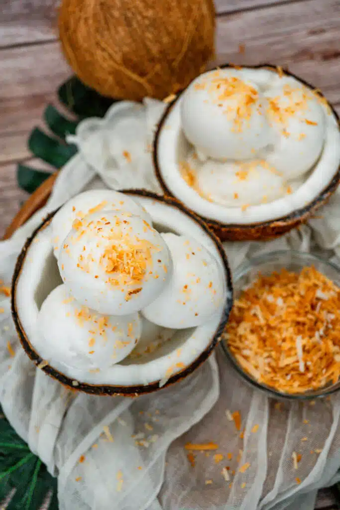 Two fresh coconut shells filled with four scoops of homemade Coconut Sorbet with toasted coconut on top.