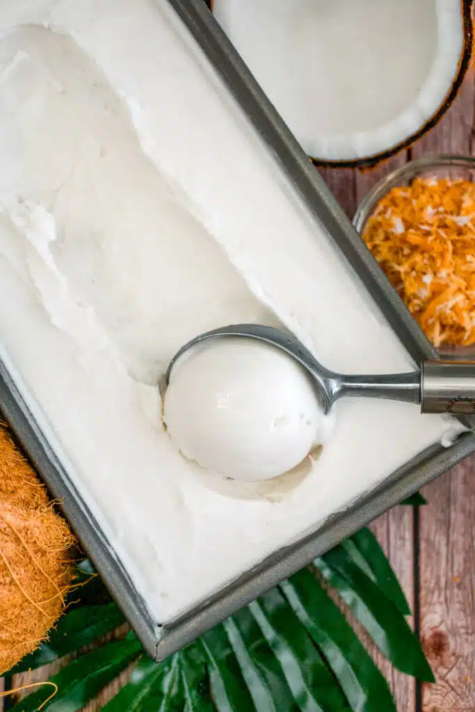 An ice cream scooper getting a perfect scoop of Coconut Sorbet from a rectangle baking dish.