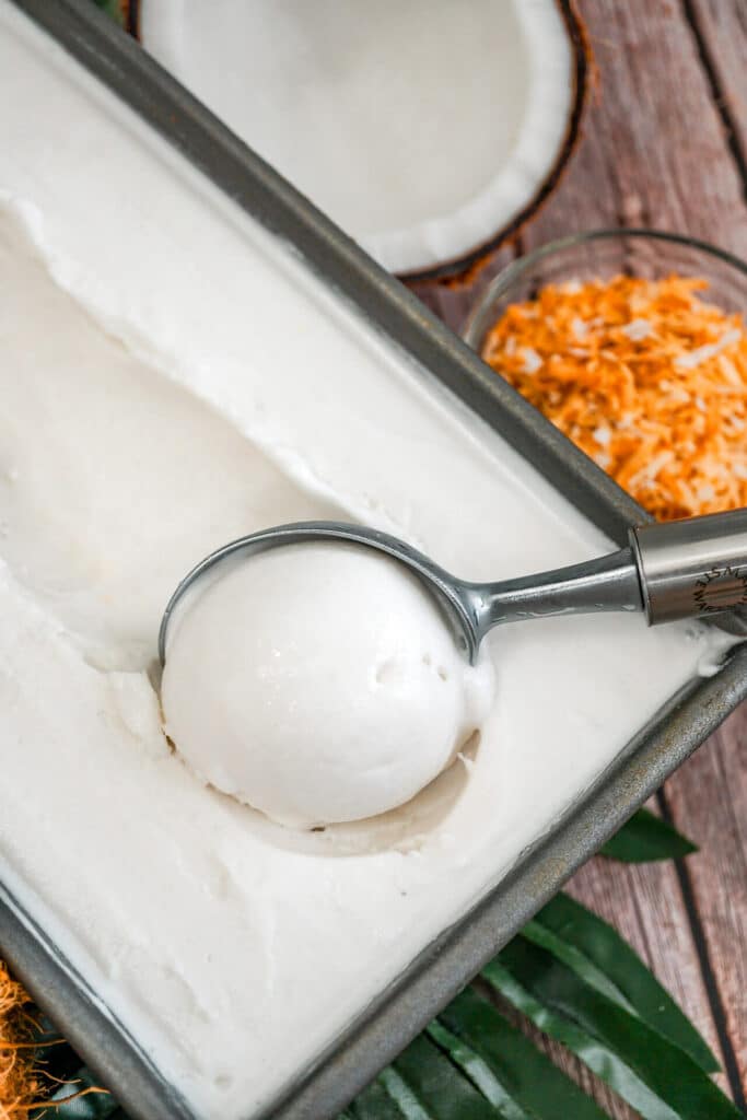 An ice cream scoop getting a scoop of homemade Coconut Sorbet from a rectangle baking pan.