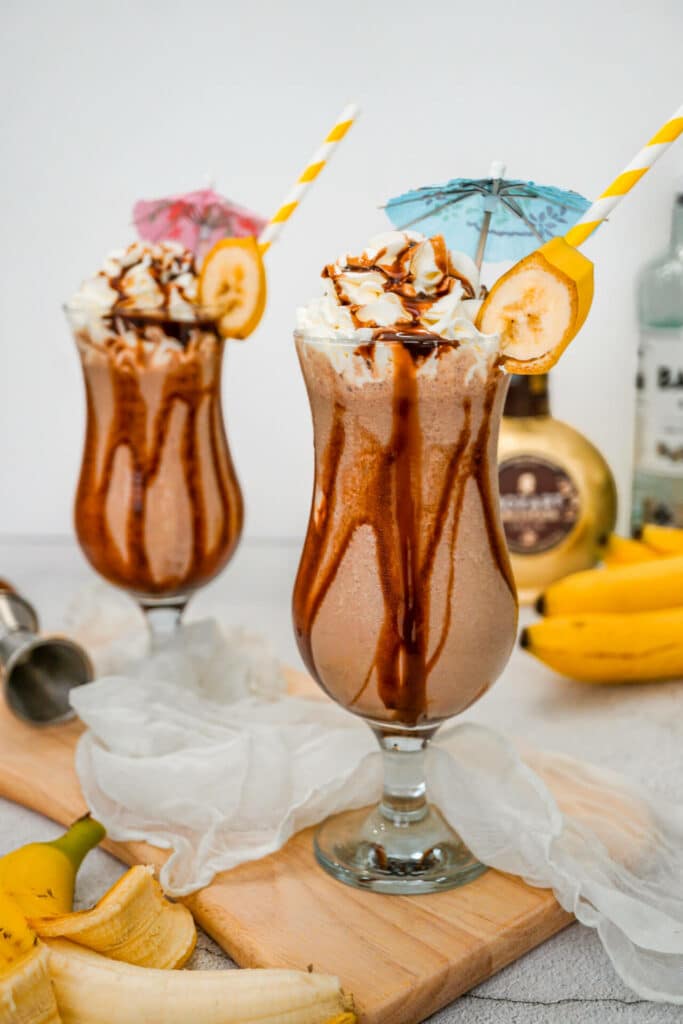 Two hurricane glasses filled with a Dirty Monkey Frozen cocktail made with chocolate liqueur.