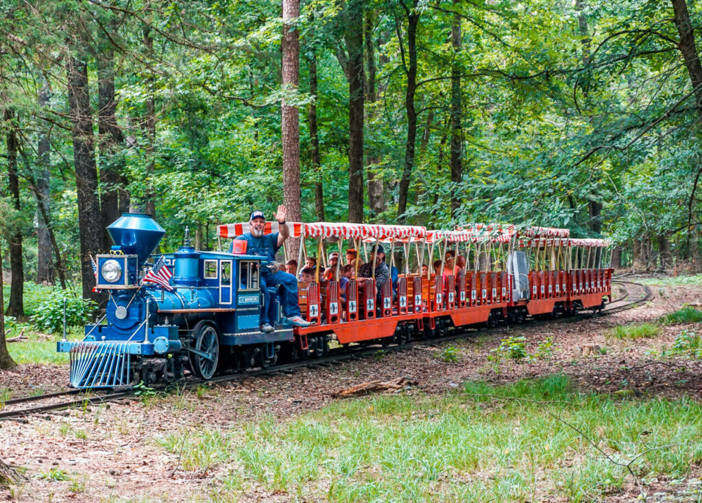 A blue engine train with a conductor waving and red and white seats from Beavers Bend Depot in Broken Bow.