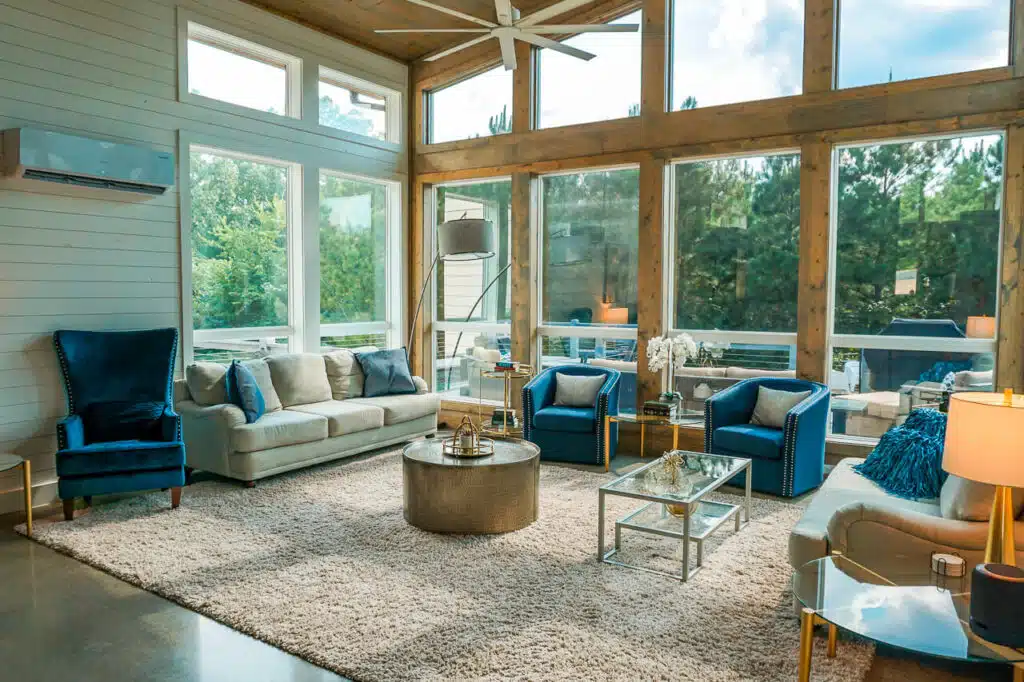 Inside a luxury cabin in Broken Bow, Oklahoma. A gorgeous modern-styled living room with floor to ceiling windows, blue and beige sofa chairs. 