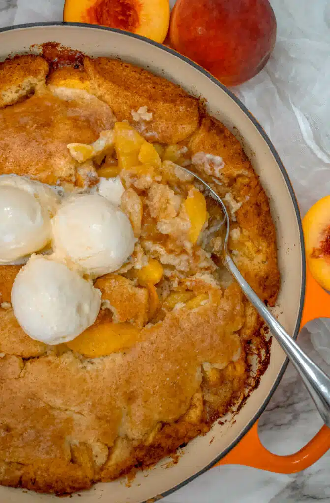 A spoon digging into a juicy peach cobbler baked in a Dutch oven.