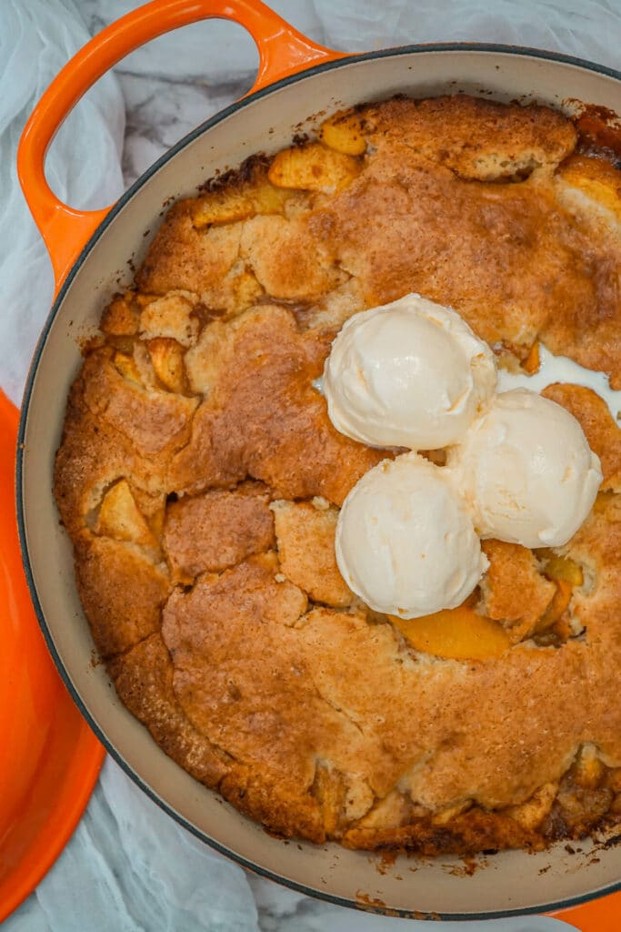 A Dutch-oven peach cobbler with vanilla ice cream melting on top.