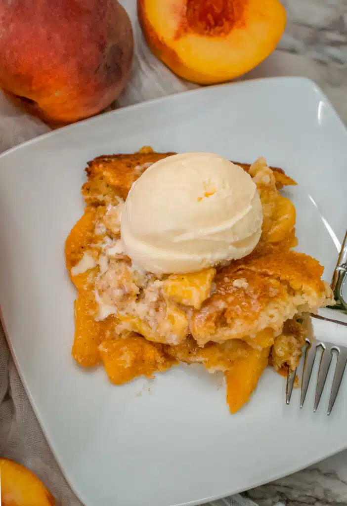 A portion of Southern-style peach cobbler on a white plate with a scoop of vanilla ice cream on top.