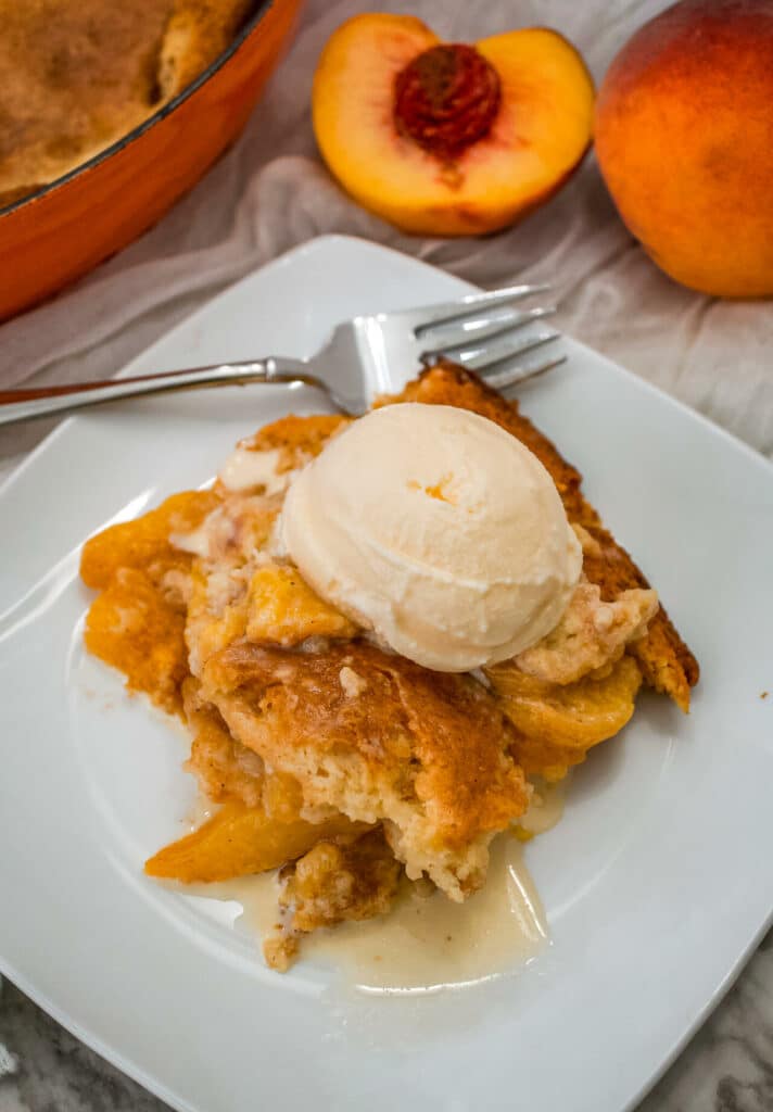 A portion of Southern-style peach cobbler on a white plate with a scoop of vanilla ice cream on top.