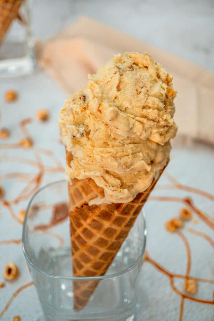 A glass holding a waffle cone filled with scoops of homemade Hazelnuts Salted Caramel Ice Cream. 