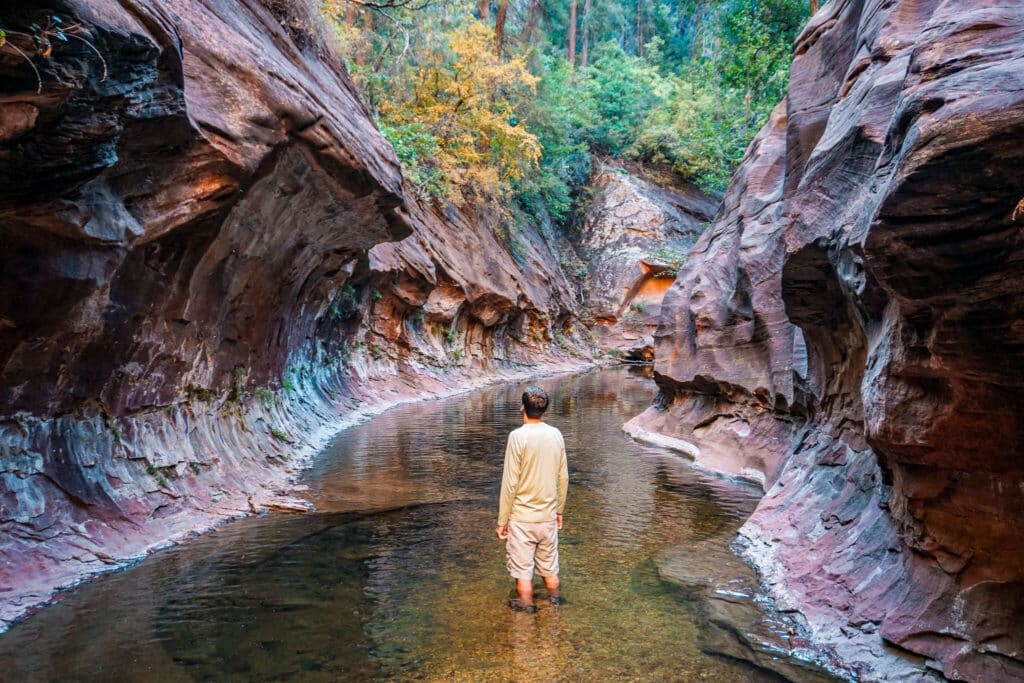 A man knee-deep in a creek inside a slot canyon from the West Fork of Oak Creek Trail in Sedona.