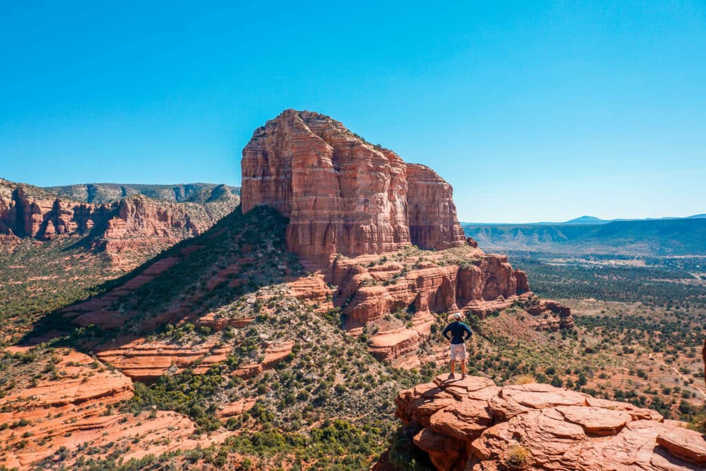 A man standing on the edge of a summit at Bell Rock admiring the red rock butte and beautiful landscape. 