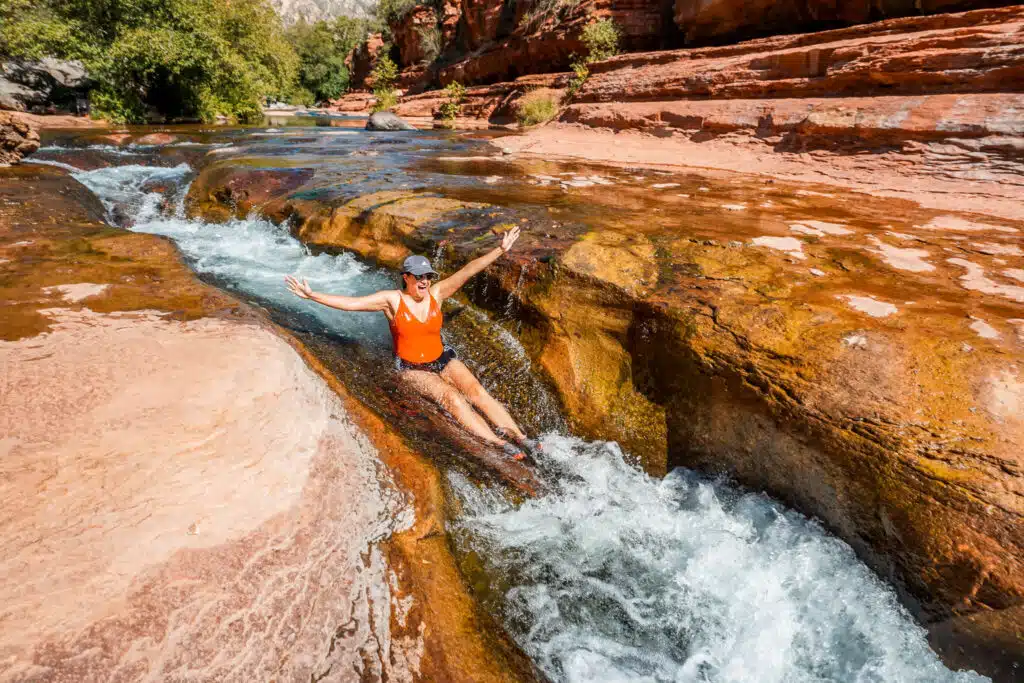 A woman in an orange bathing suit sliding down the natural water slide at Slide Rock State Park—one of the best things to do in Sedona.