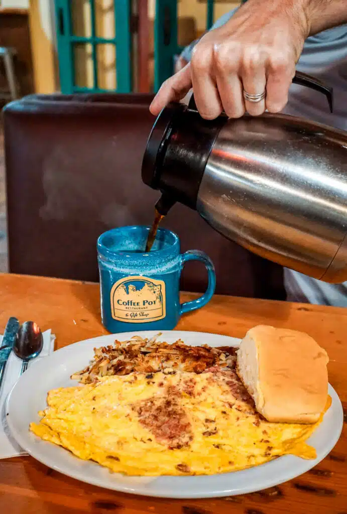 Someone pouring coffee from a coffee pot into a mug next to a plate of hash browns and an omelette at the Coffee Pot Restaurant in Sedona. 