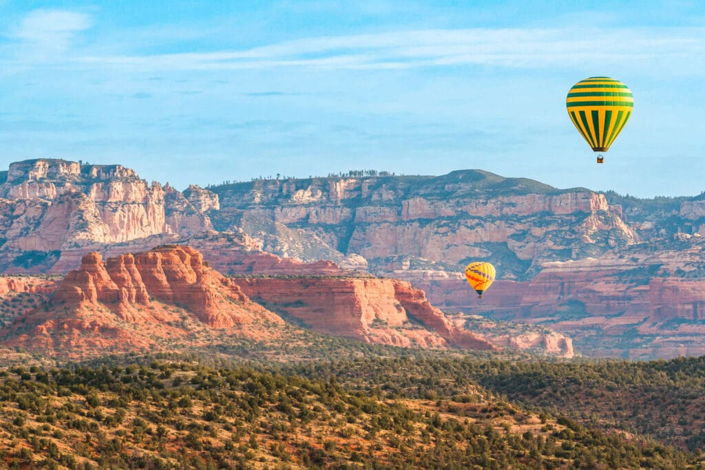 Two yellow hot air balloons floating in the sky above the red rock landscape—an ultimate bucket list experience for a 3-day Sedona Itinerary.