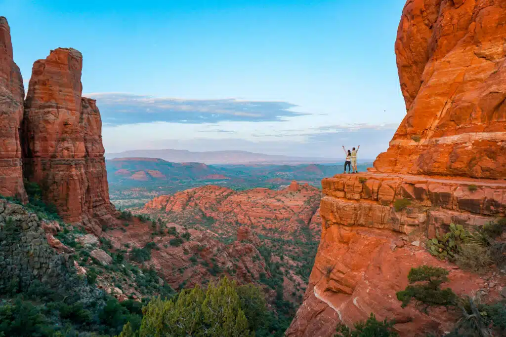 A couple on the edge of a butte at Cathedral Rock enjoying gorgeous views during sunrise.