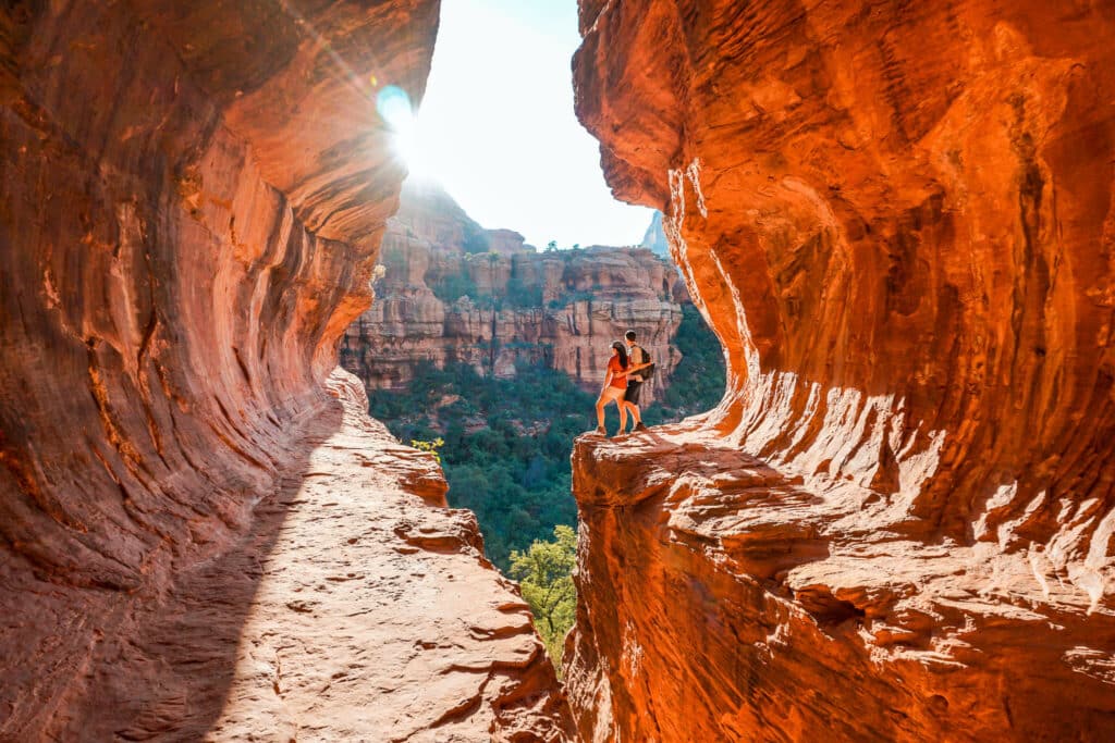 A couple at the edge of Subway Cave looking out into the canyon during sunrise.